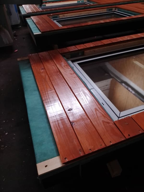 Close view of a panel face on the factory floor: stained wood boards, edge tape and a glazed window set into the panel