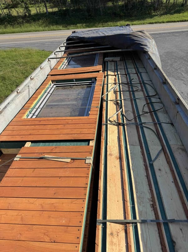 Looking down into the open-top container at strapped wood-clad wall panels with their windows fitted