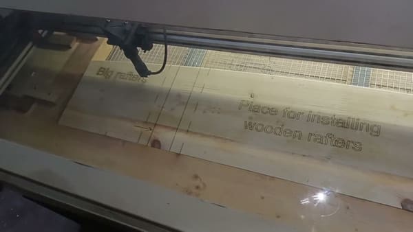 A CNC laser gantry engraving a rafter label into a glulam segment