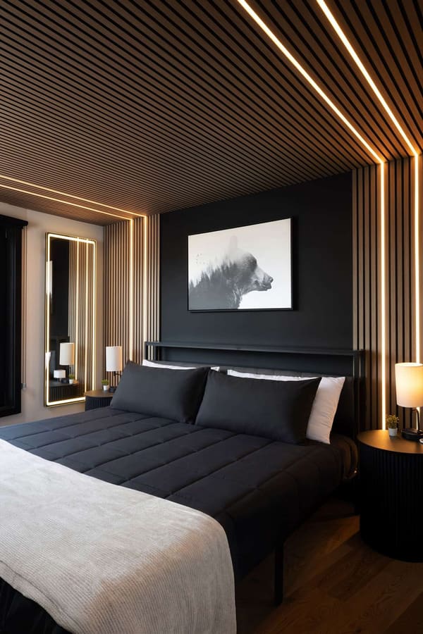 A bedroom with a slatted wood ceiling and walls, strip lighting, a dark feature wall with a bear print and a king bed